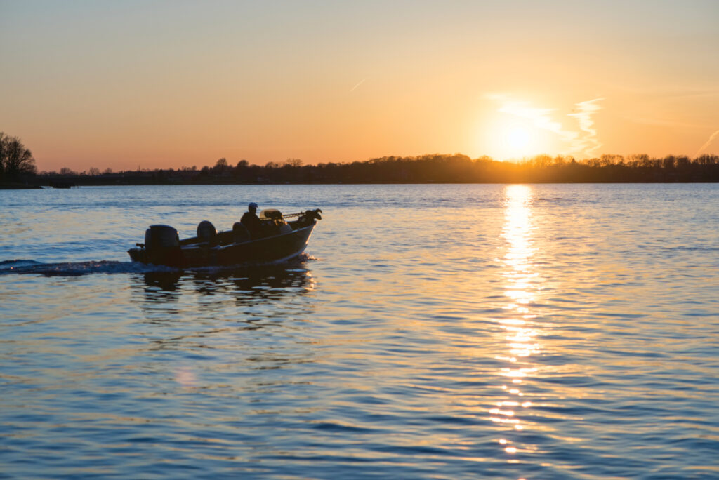 Silhouette of fishing boat and person on a Minnesota lake during the sunset with clouds and sun reflection on the lake water. This picture was taken during the early part of summer.