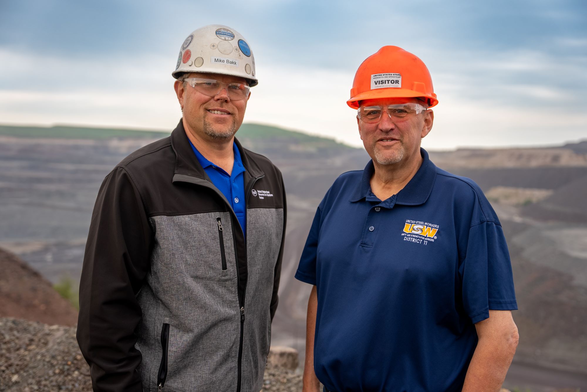 Iron Ore Alliance co-chairs Mike Bakk and John Arbogast post in hardhats in front of an iron mining pit