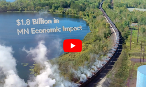 An aerial shot of train tracks near a mine on the Iron Range with the words "$1.8 billion in MN Economic Impact" and the YouTube play icon